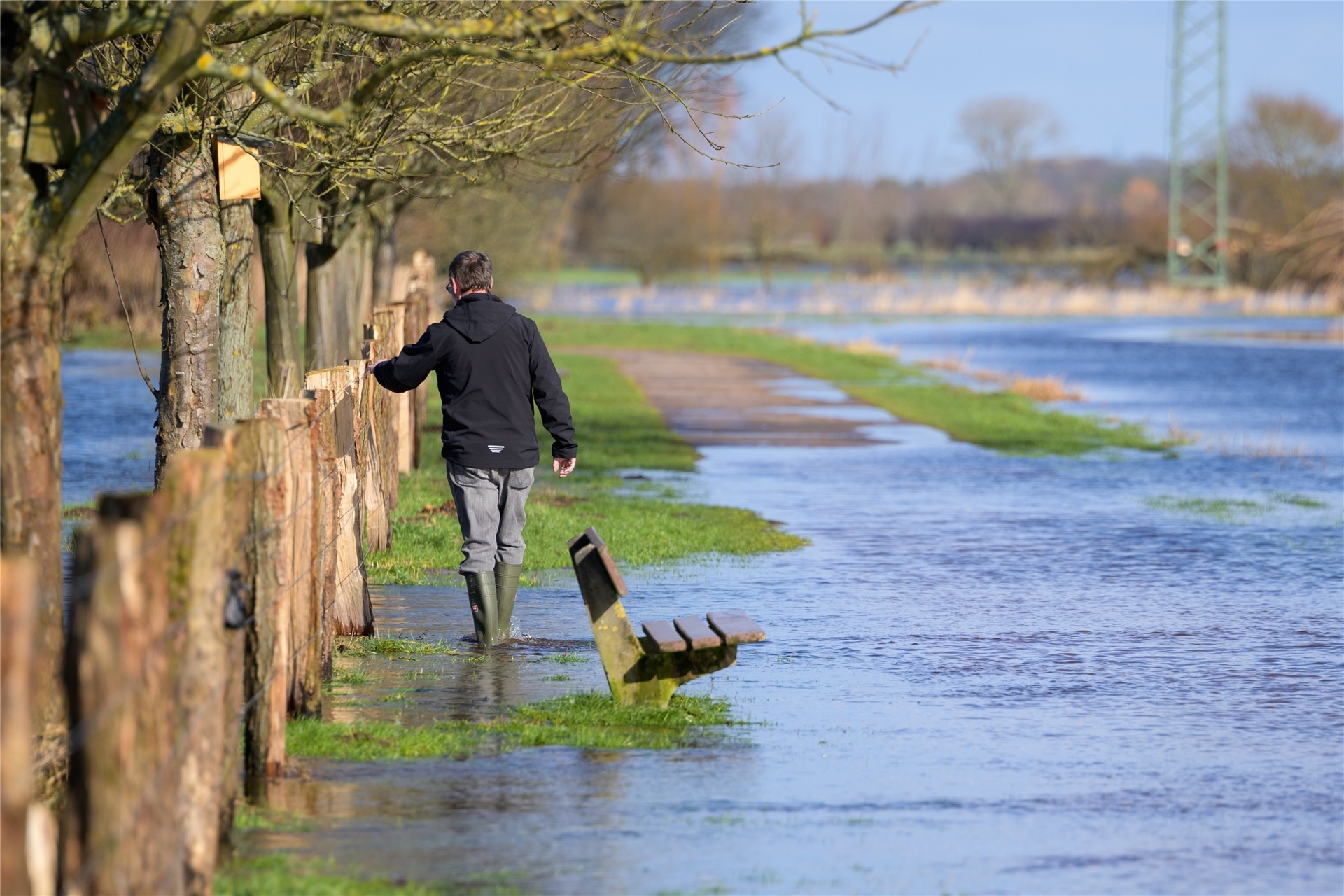 Ein Mann watet mit Gummistiefeln durch das Wasser der über die Ufer getretenen Pinnau. Noch sind viele Felder und Wiesen überschwemmt und nicht alle Straßen wieder trocken. Hochwasser-Situationen könnten durch den Klimawandel öfter auftreten.