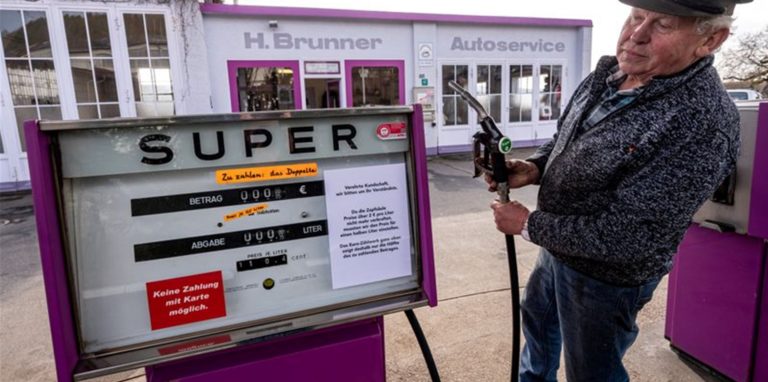 Hans Brunner steht an einer Zapfsäule seiner Tankstelle. Die Tankstelle zeigt Benzin- und Dieselpreise halbliterweise an.