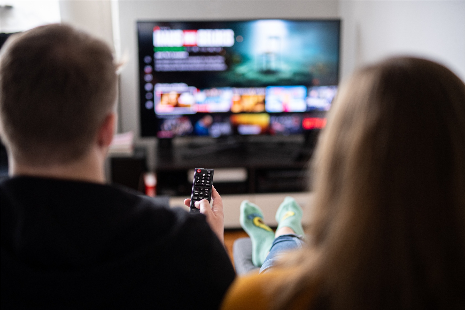 Ein Paar sitzt vor dem Fernseher, der Mann hält die Fernbedienung.