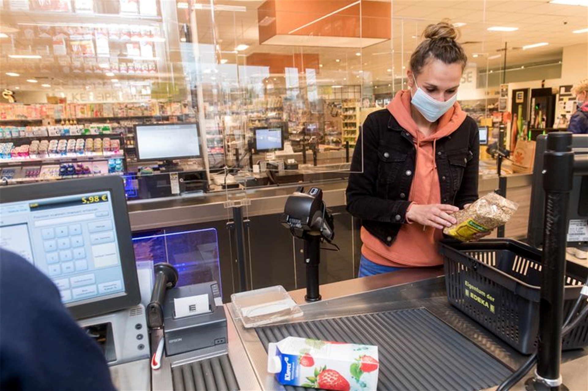 Eine Frau steht an der Kasse im Supermarkt und packt ihre Einkäufe ein. Sie trägt Maske.