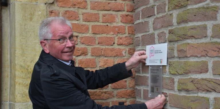 Hubertus Erfmann vom Kirchenvorstand platzierte neue Schilder an der St.-Anna-Kirche. Diese informieren über die Kapelle und weisen auf die Fördermittel für die Beleuchtung hin.