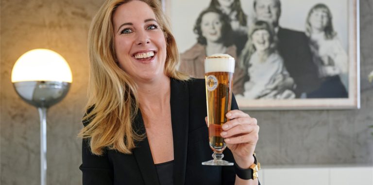 Catharina Cramer, Inhaberin des Brauerei-Unternehmens Warsteiner, sitzt mit einem Glas Bier in ihrem Büro. Im Hintergrund hängt ein Familienfoto, auf dem sie bei ihrem Vater Albert auf dem Schoß sitzt.
