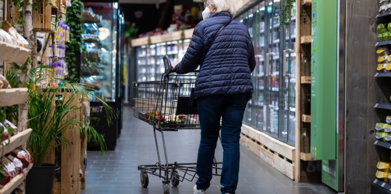 Eine Frau geht mit ihrem Einkaufswagen durch einen Supermarkt.