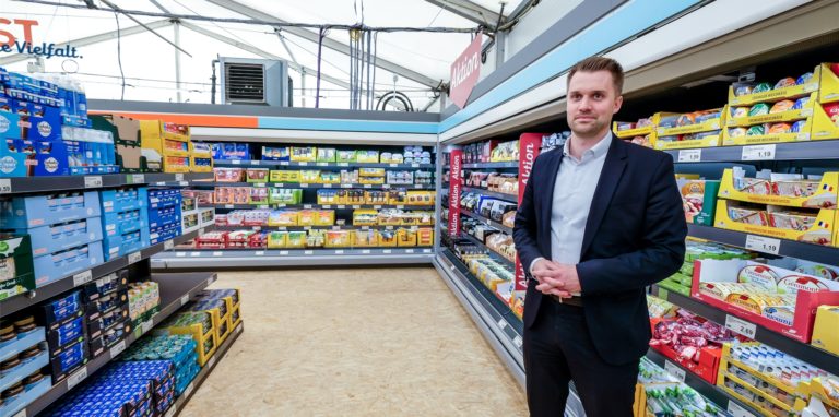Eine seltene Zelt-Filiale des Discounters Aldi Nord in Recklinghausen. Die Regale sind gefüllt. Neben der Tiefkühltheke steht ein Mann im schwarzen Anzug: Lukas Klunke, „Leiter Verkauf“ bei Aldi Nord.