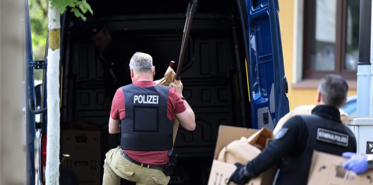 Polizisten tragen Gegenstände, darunter mehrere Stichwaffen und Speere, aus dem Wohnhaus des Verdächtigen.