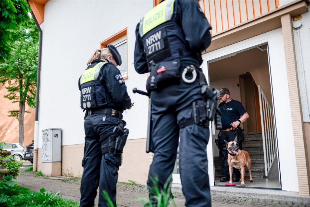 Ein Polizist mit Spürhund steht im Hauseingang des Tatverdächtigen in Essen.
