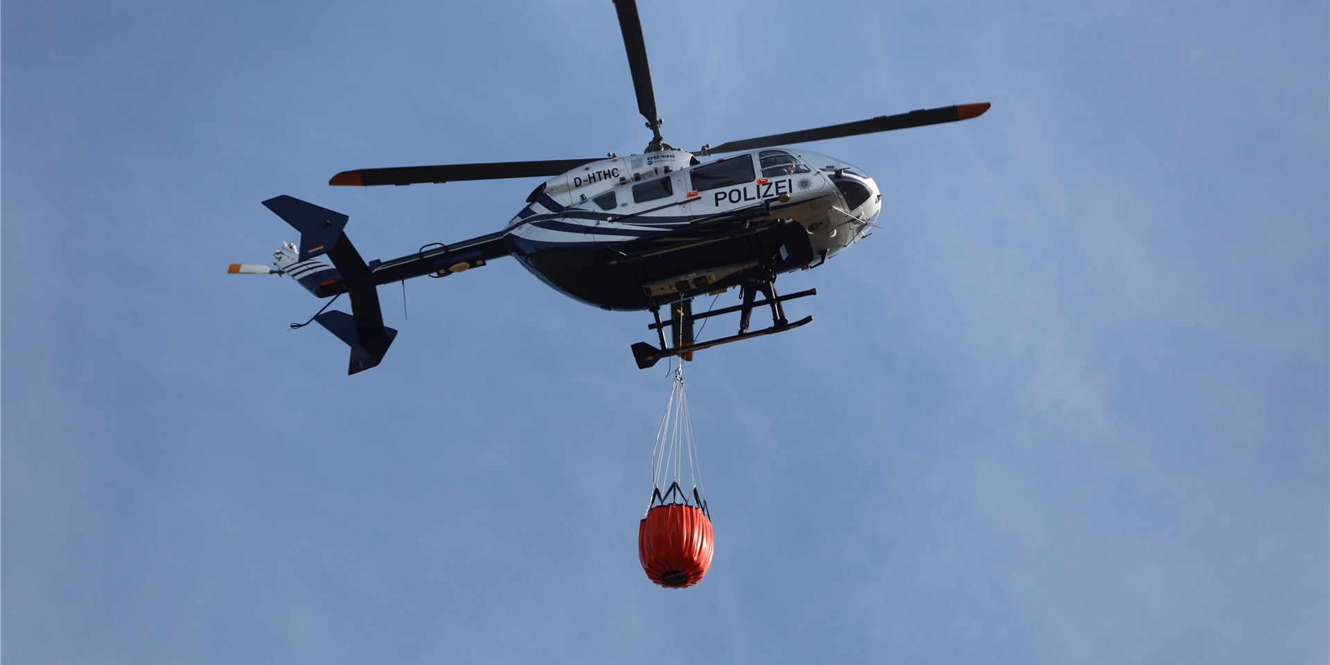 Ein Polizeihubschrauber bringt Wasser zum Löschen an einen Waldbrand bei Stiege im Harz.