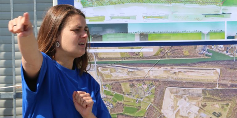 Verena Speer vor einer Illustration für den Zukunftsgarten, der zwischen der Halde Großes Holz und der Wasserstadt Aden entsteht. Die Projektleiterin erklärt Besuchern, was dort geplant ist.