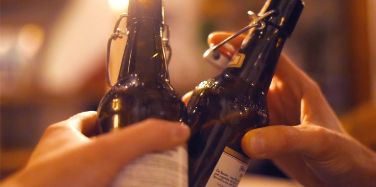 Zwei Personen stoßen in einer Kneipe mit Bier in der Flasche an.