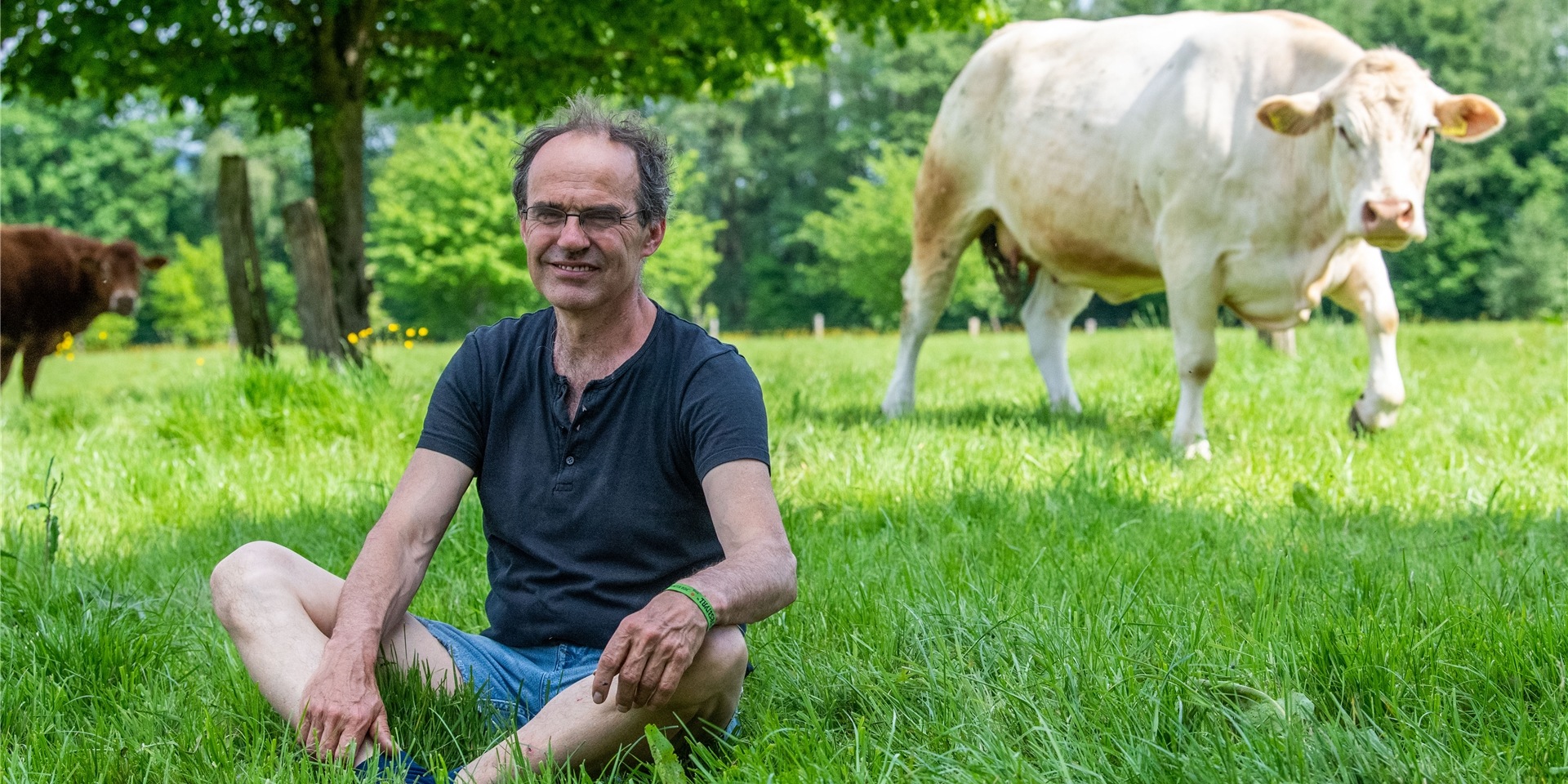 Ulf Allhoff-Cramer, Landwirt, sitzt auf einer Weide neben einer von seinen Kühen. Der Bio-Bauer macht den Autokonzern VW mitverantwortlich für Schäden an seinem Hof. Er will zusammen mit Greenpeace vor Gericht erreichen, dass VW bis 2030 keine Verbrennungsfahrzeuge mehr herstellt.