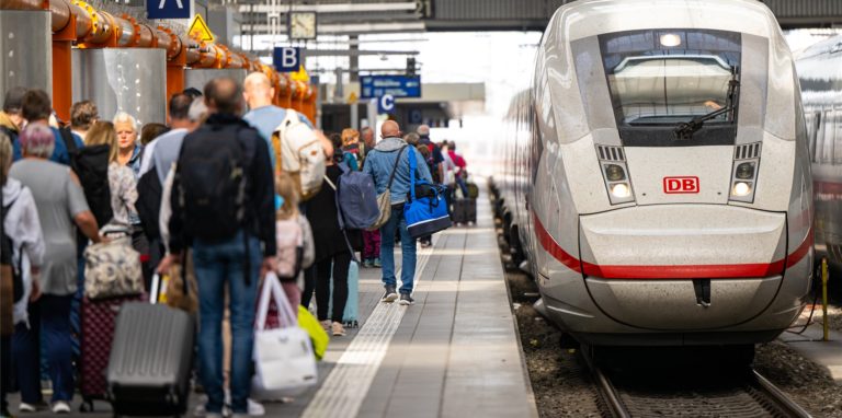 Reisende stehen am Hauptbahnhof in München an einem Bahnsteig und warten auf die Einfahrt ihres Zugs.