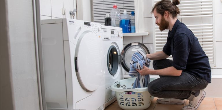 Ein Mann packt Wäsche in die Waschmaschine.