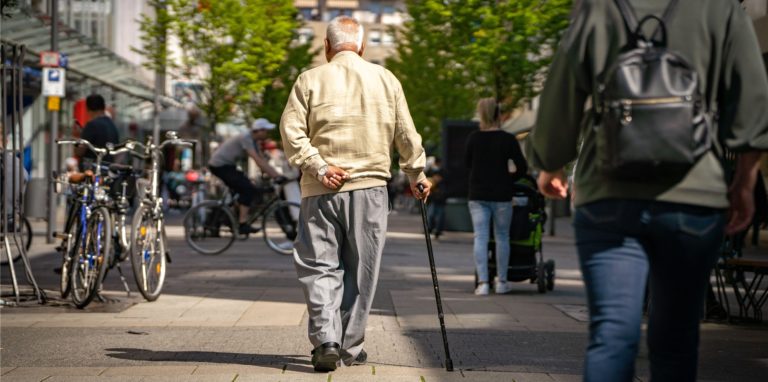 Ein älterer Herr spaziert mit einem Gehstock durch die Straße.
