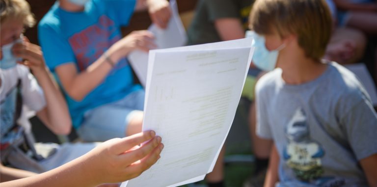 Ein Kind hält am letzten Schultag vor den Sommerferien ein Zeugnis in den Händen.