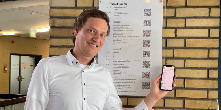 Smart City Koordinator Gregor Spanke präsentiert eine simple und zugleich geniale Maßnahme: Damit auch Bürgerinnen und Bürger ohne gute Deutschkenntnisse den Weg in die richtige Etage finden, können die Orientierungs-Tafeln im Rathaus nun mit dem Handy in acht Sprachen übersetzt werden.