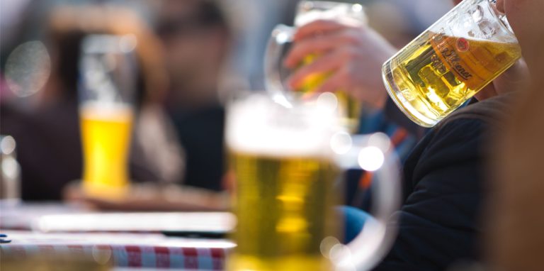 Menschen trinken Bier an Tischen draußen in der Gastronomie.