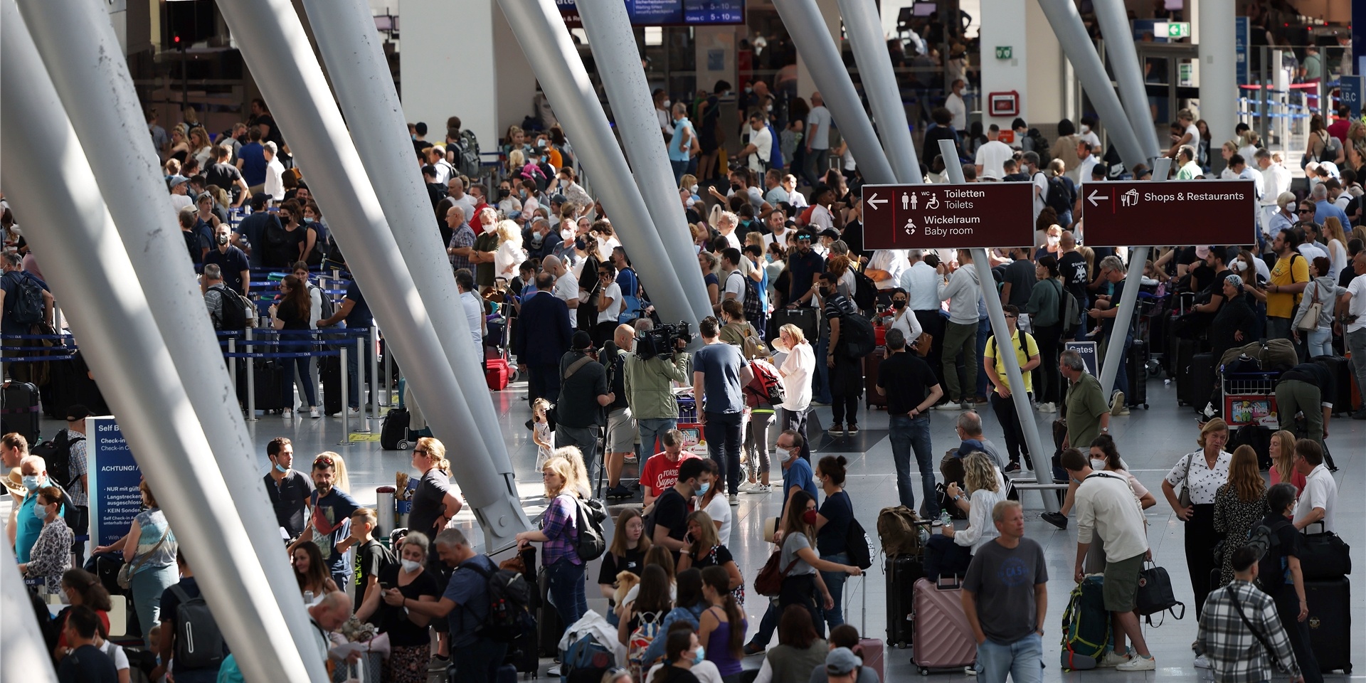 Passagiere stehen im Flughafen Düsseldorf in Schlangen und warten auf ihre Abfertigungen.