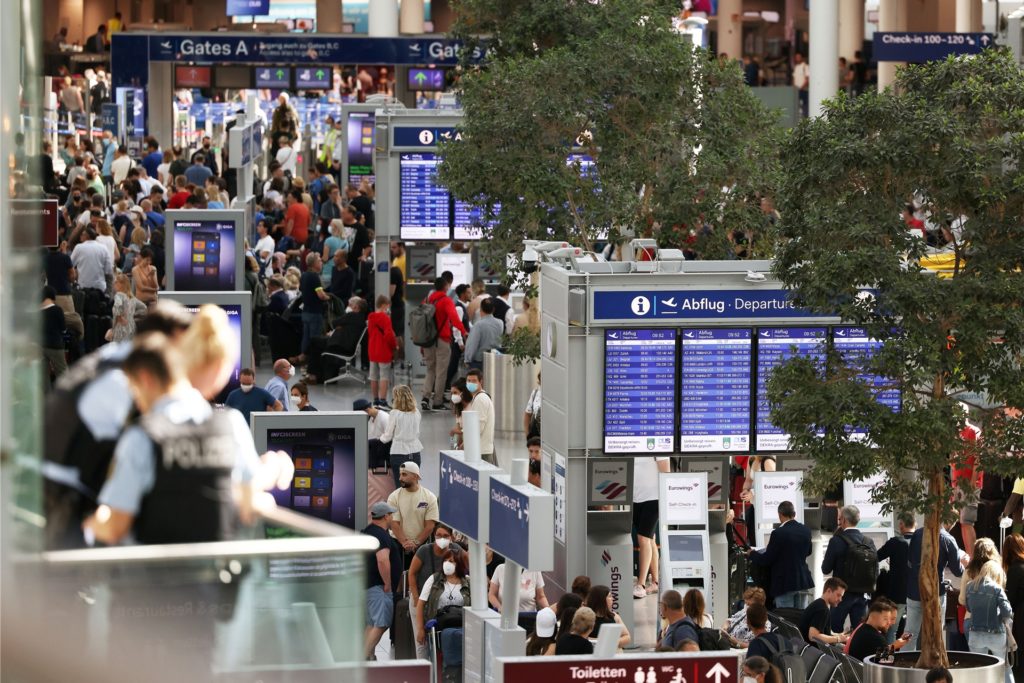 Passagiere stehen im Flughafen Düsseldorf in Schlangen und warten auf ihre Abfertigungen.