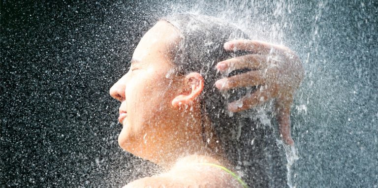 Eine Frau steht im Wassernebel unter der Dusche im Freibad.