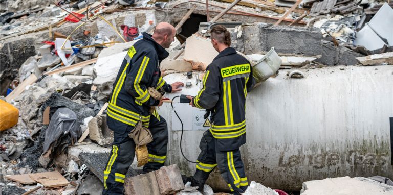 Feuerwehrleute machen eine Messung an einem Gastank zwischen den Trümmern.