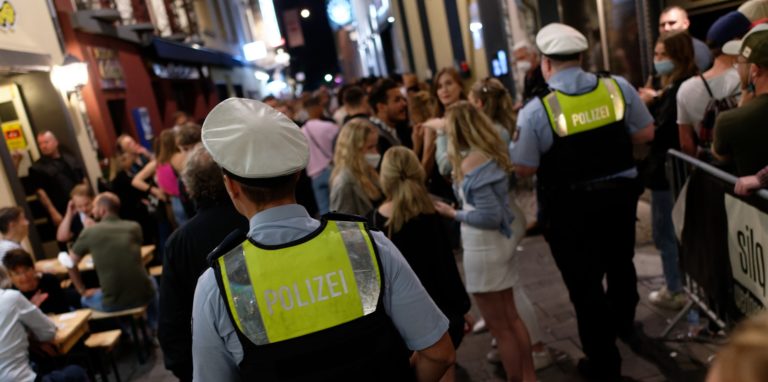 Polizisten stehen in der Düsseldorfer Altstadt vor feiernden Menschen.