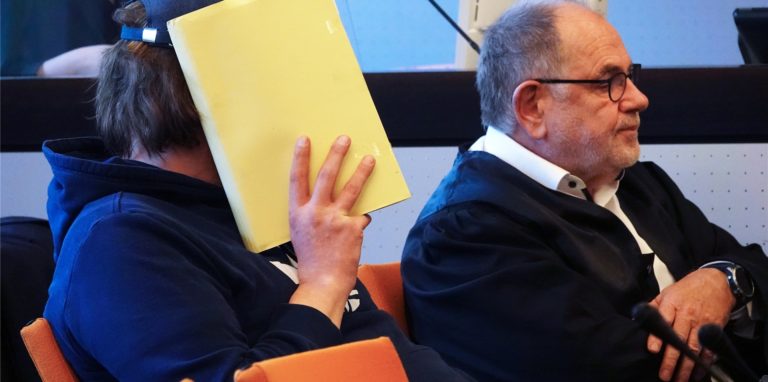 Einer der beiden Angeklagten (l), der sich im Saal des Landgerichts eine Mappe vor das Gesicht hält, sitzt neben seinem Anwalt.