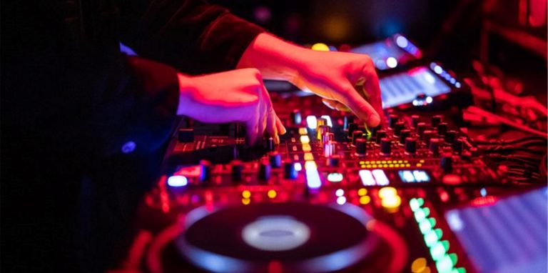 Ein DJ steht in einem Club am Mischpult.