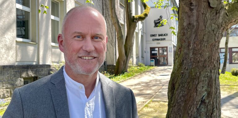 Schulleiter Ulrich Schmitz steht lächelnd vor dem Ernst-Barlach-Gymnasium.