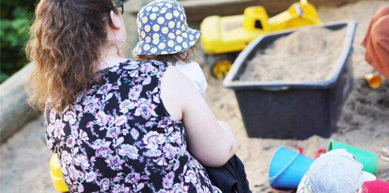 Eine Frau sitzt mit einem Kind im Sandkasten.
