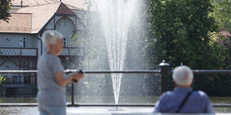 Besucher sitzen auf einer Bank vor einer Wasserfontäne im Forellenteich.