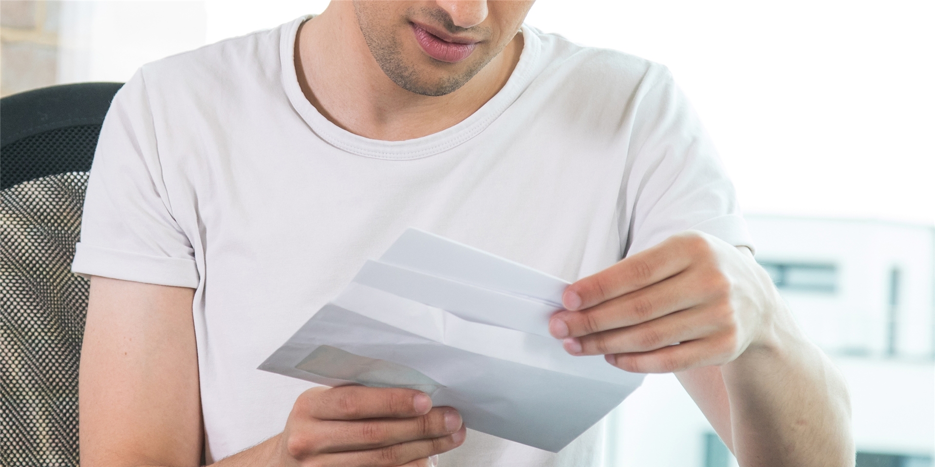 Ein Mann sieht an einem Tisch Briefe durch, die er in der Hand hält