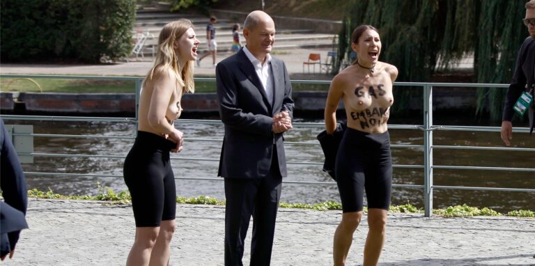 Zwei Frauen stehen neben Bundeskanzler Olaf Scholz (SPD) und haben den Slogan «Gas Embaro now» auf dem Oberkörper stehen