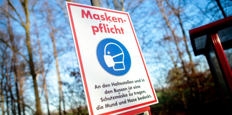 Ein Schild mit der Aufschrift „Maskenpflicht“ hängt an einer Bushaltestelle