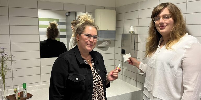 ​Schüler-Vertretungslehrerin Lara Stadtmann (l.) und Schülersprecherin Jocelyn Ahlrichs (r.) vor dem Spender der Damenhygieneartikel im Lippe-Berufskolleg Lünen.