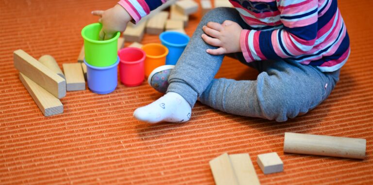 Ein Kind sitzt auf dem Boden und spielt mit Bechern und Holzklötzen.