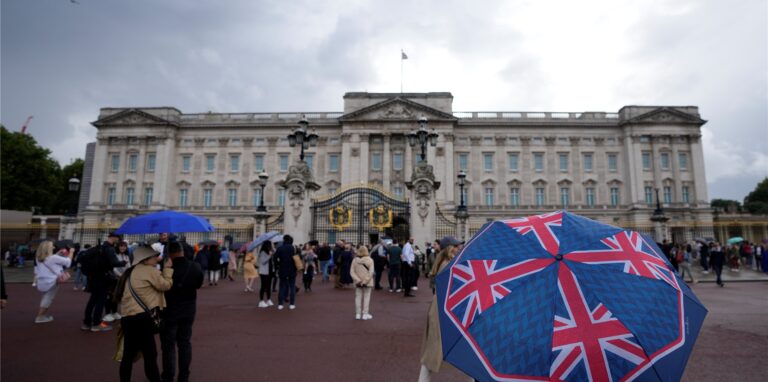 Zwei Personen gehen in einer Ausstellung im Buckingham Palast an Plakaten vorüber, auf denen Königin Elizabeth II. abgebildet ist.