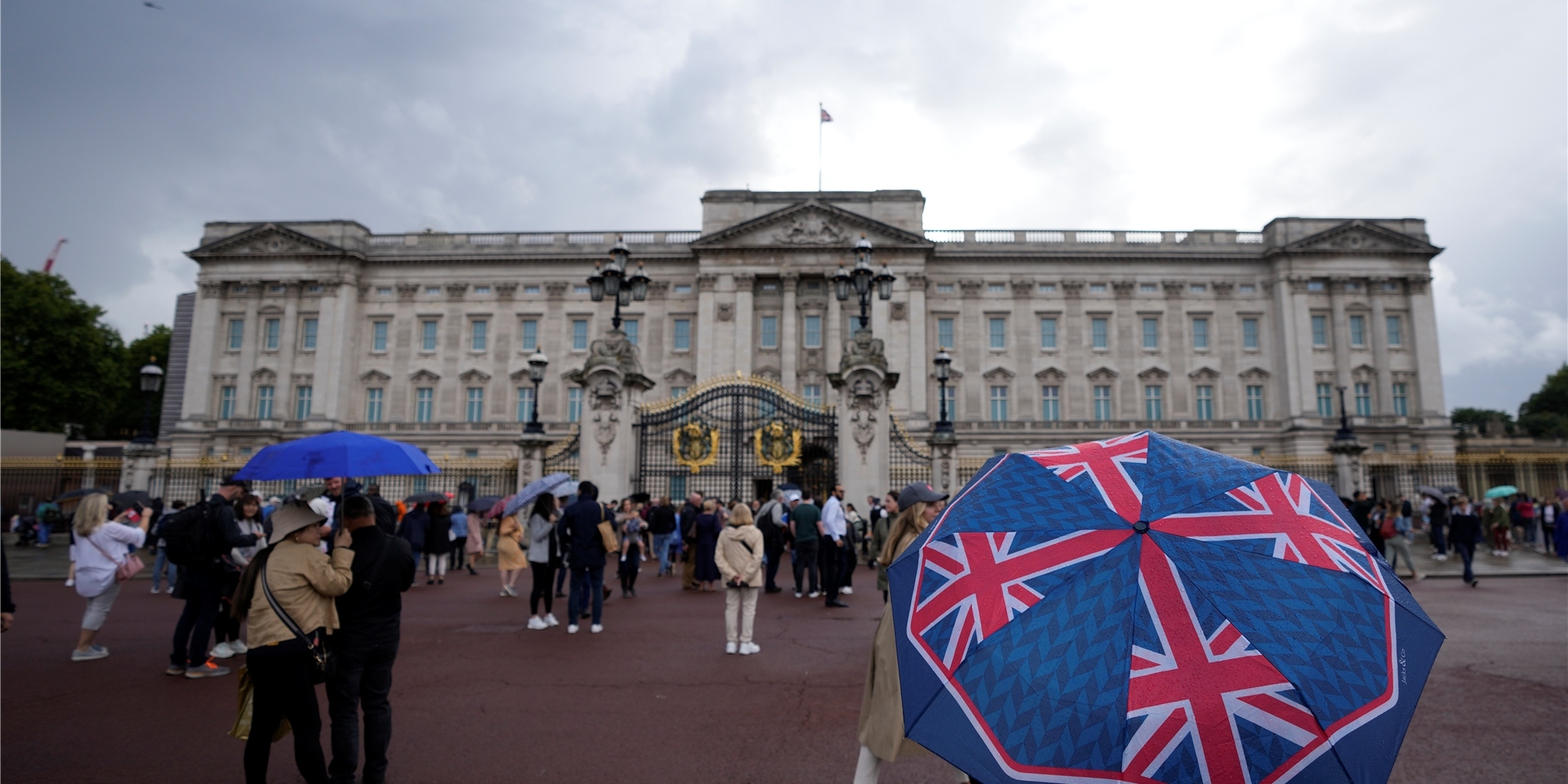 Zwei Personen gehen in einer Ausstellung im Buckingham Palast an Plakaten vorüber, auf denen Königin Elizabeth II. abgebildet ist.