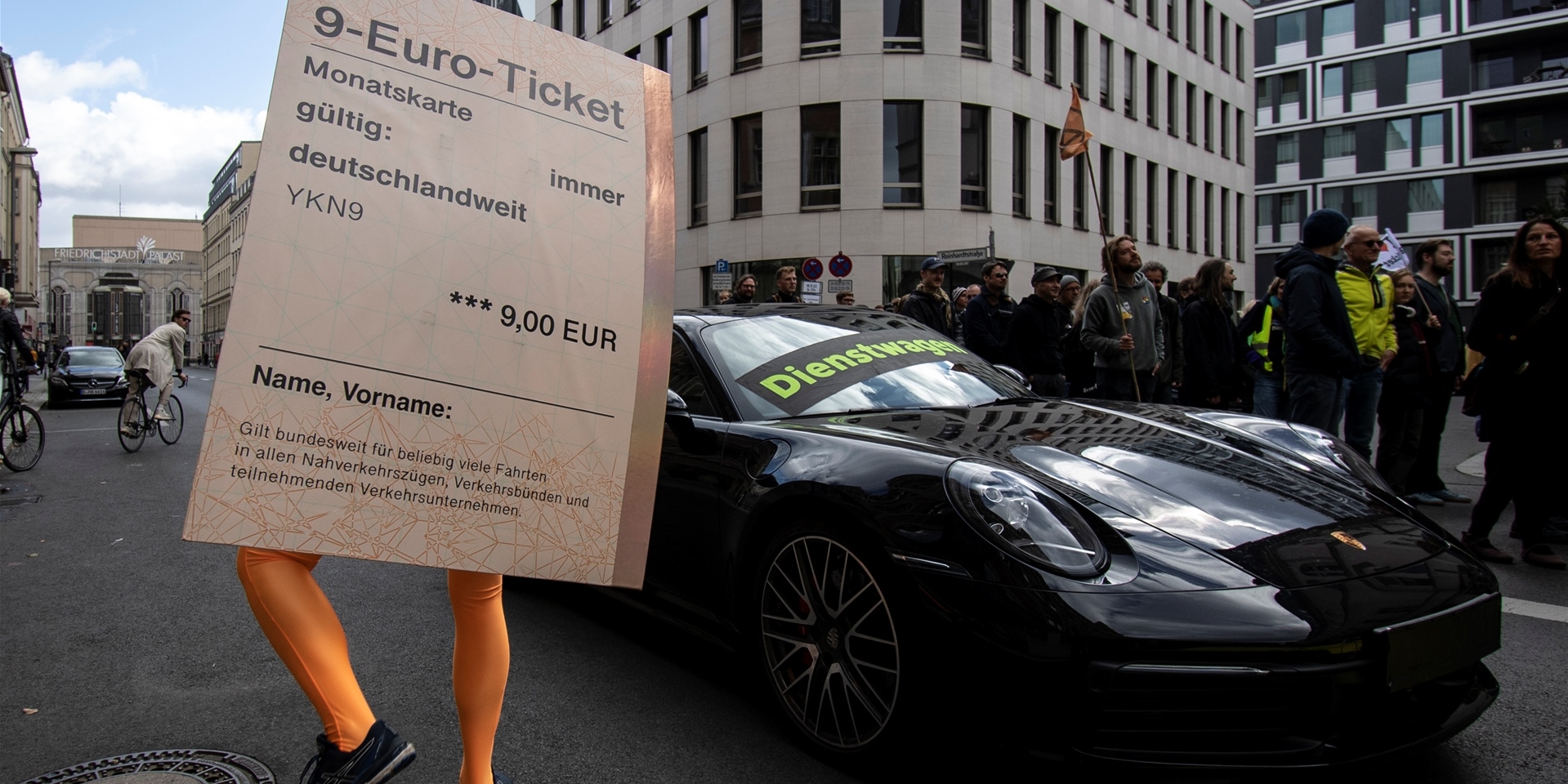 „Dienstwagen“ steht auf einem Porsche 911 während ein Demonstrant mit einem übergroßen „9-Euro-Ticket“ bei einer Protestaktion der Umweltschutz-Organisation Greenpeace vor der FDP-Bundeszentrale daneben steht.
