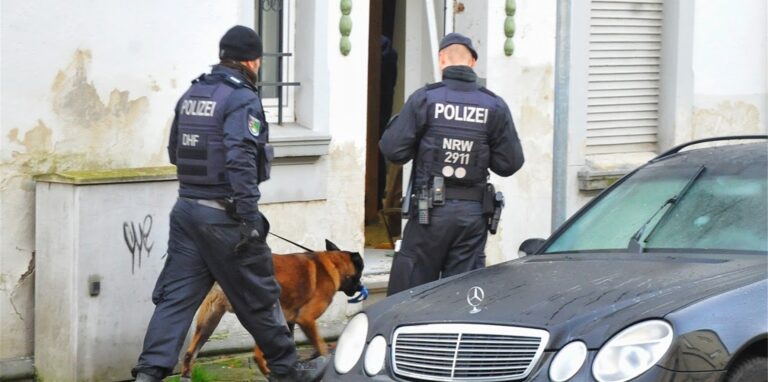 Zwei Polizisten stehen vor einem Haus.