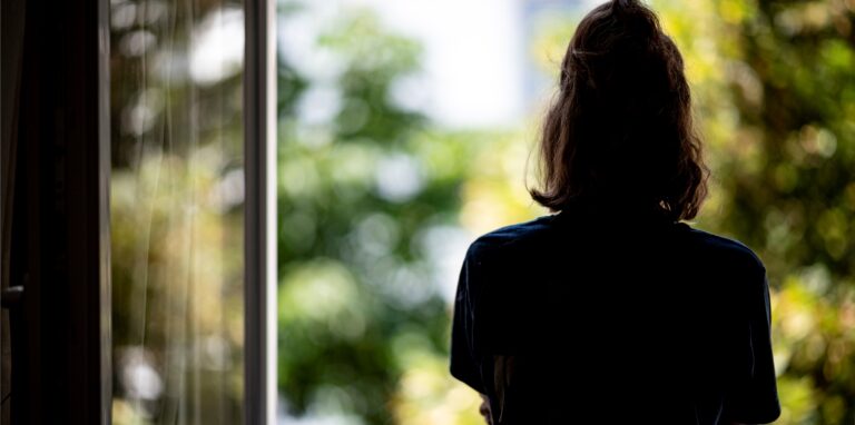 Eine Frau steht in ihrer Wohnung am Fenster.