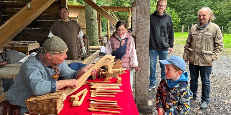 Holzschnitzer Hans Koehn zeigt Emilia und Vincent, wie er ein Steckenpferd anfertigt. Beim Handwerkerfest im Römerpark versetzten Handwerker die  Besucher in die Wikinger-, Germanen- und Römerzeit.