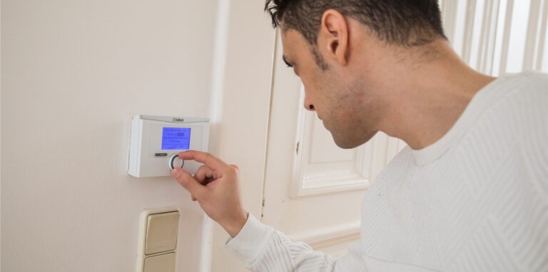 Ein Mann regelt die Temperatur seiner Heizung an einem Thermostat