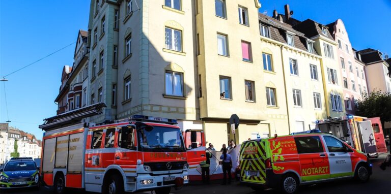 Rettungskräfte und Einsatzfahrzeuge stehen vor dem Mehrfamilienhaus, aus dem das Kind stürzte.