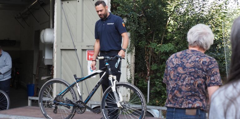 Ein Mann steht mit einem Fahrrad, das versteigert werden soll, auf einer Art Bühne.