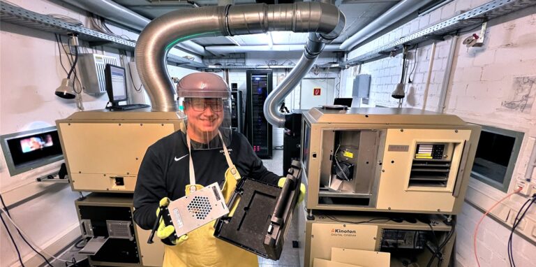 Sven Hilbk trägt eine Schürze, Handschuhe und einen Augenschutz. Dabei hält er eine Festplatte in die Kamera.