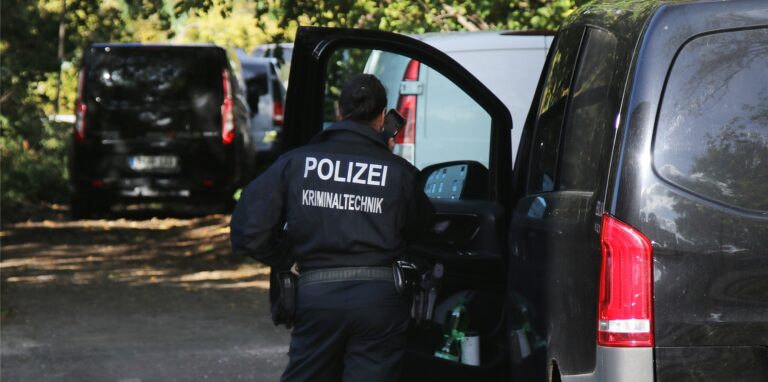 Eine Kriminaltechnikerin steht in der Nähe vom S-Bahnhof Hohenschönhausen neben Fahrzeugen der Polizei.