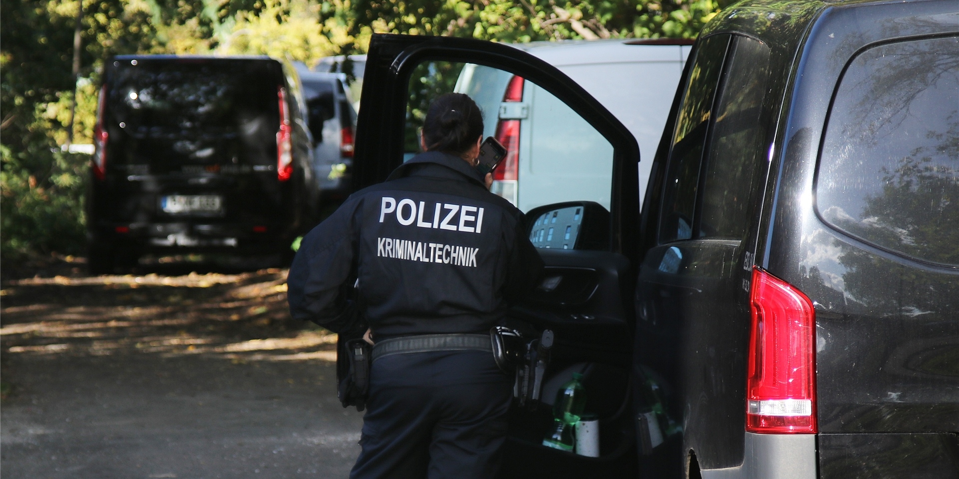 Eine Kriminaltechnikerin steht in der Nähe vom S-Bahnhof Hohenschönhausen neben Fahrzeugen der Polizei.