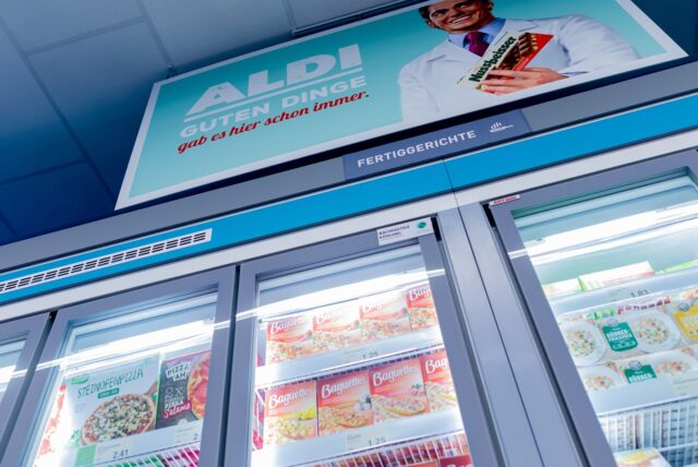 Schilder mit historischen Motiven hängen über dem Tiefkühlbereich mit Fertiggerichten im „neuen ältesten Aldi Markt“.