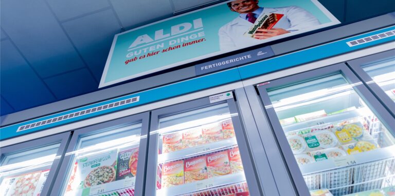 Schilder mit historischen Motiven hängen über dem Tiefkühlbereich mit Fertiggerichten im „neuen ältesten Aldi Markt“.