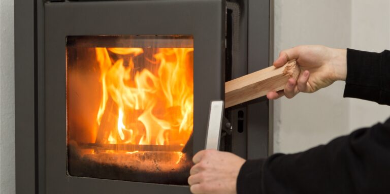 Eine Person legt ein Stück Holz in einen Kaminofen